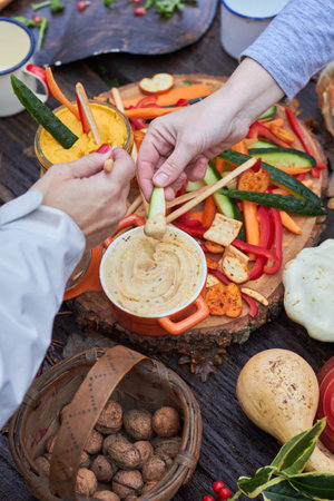 hands dipong veggies in humus on a rustic table