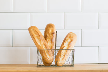 bread baguettes on a basket on a wooden table, white tile background in a bakeryの写真素材