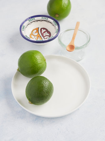 pair of whole limes in a white plate, ready to use it on drink or foodの写真素材