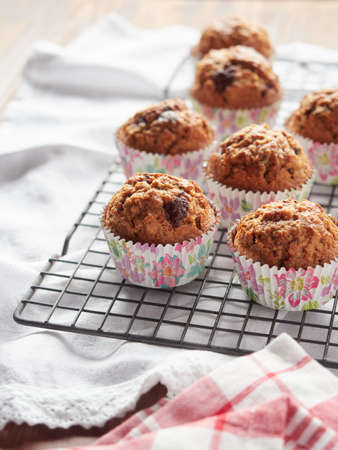 Freshly baked homemade cupcakes in colored molds on a cooling rack, on the table with kitchen clothsの写真素材