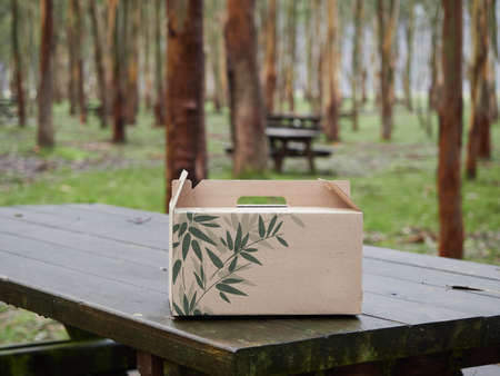 cardboard box with green leaves on a wooden picnic table in a forest with trees in the background, autumn or winter. Plastic free, zero waste and sustainable packaging conceptの写真素材