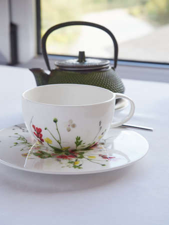 white tea cup decorated with painted flowers and oriental teapot in front of a white windowの写真素材