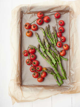 group of veggies on a baking parchment, cherries tomatoes and asparragus uncooked ready to homemade rosted bakingの写真素材