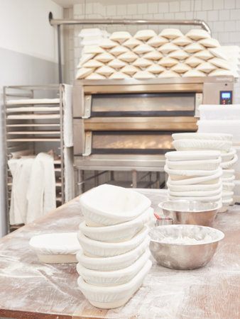 scene inside a bakery: work table for kneading bread with stacked bread pans and flour bowls, ovens...