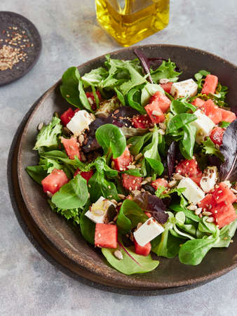 Fresh summer watermelon salad with feta cheese and green leafy, dressed with olive oil and seedsの写真素材