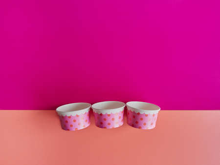 three ice cream cups with empty colored polka dots isolated on fuchsia and orange background. strong color paletteの写真素材