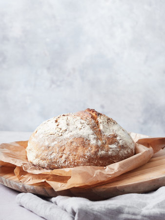 rustic loaf of sourdough bread on baking paper on a wooden board. gray background