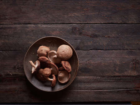 fresh whole shiitake mushrooms, lentinula edoes, on a dark plate on a dark wooden table, top view with copy spaceの写真素材