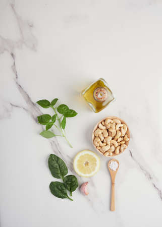 top view of a marbel kitchen table with ingredients to prepare vegan pesto. Cashew, spinach, basil, garlic, salt, lemon and olive oilの写真素材