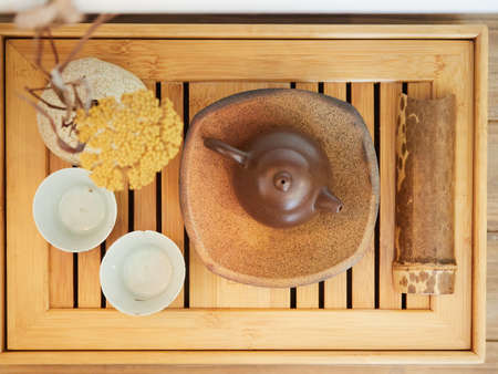 top view of asian tea set on a bamboo wood tray. Oriental style composition with yellow flowers. Brown monochromatic palette. Calm and serenity concept.の写真素材