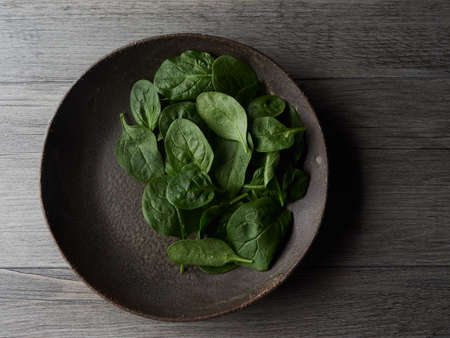 Top view of a rustic dark plate isolated with fresh spinach leaves on dark wooden table. Healthy and organic food concept.の写真素材