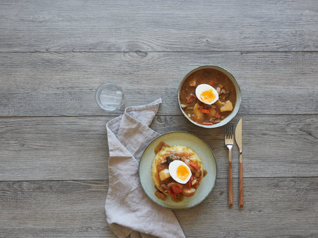 view from above of a food table with plates of mushroom and vegetable stew with poached egg halves. Cutlery and napkin for one person. Copyspace.の写真素材