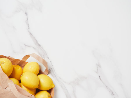 yellow lemons in paper bag placed in lower left corner on marble countertop as background, top view with copy space.の写真素材