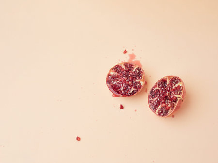 juicy pomegranate cut in half with a few drops of juice and seeds splashed isolated on a plain...