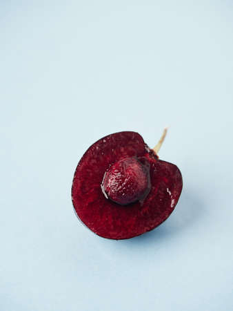 close-up view of the interior of a juicy cherry cut in half with stalk and pit on blue surface with copy spaceの写真素材