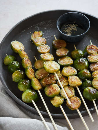 close up view of roasted brussels sprouts on skewers on a dark plate with soy sauce and sesame seeds.の写真素材
