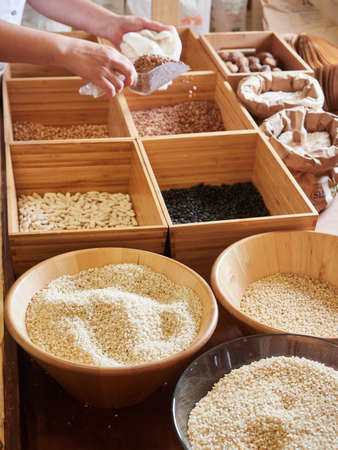 Selling food products in bulk in wooden and paper containers. Rice, legumes and flour. Purchase of products in reusable containers, filling cloth bags. Sustainable purchases in small local stores.の写真素材