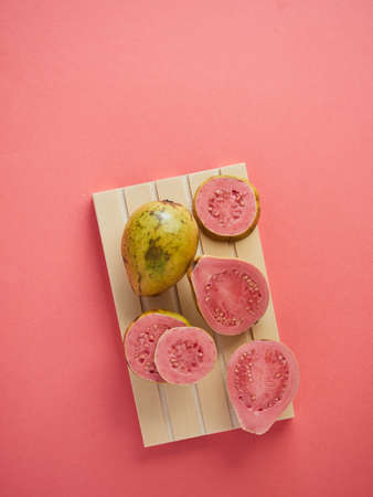 Fresh ripe whole guava, halved and sliced on a wooden tray on a pink background of the same color as the fruit pulp.の写真素材