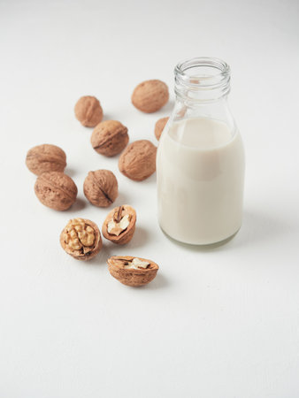 Dairy free substitute milk concept. Small glass bottle with vegetable walnut drink. Some shelled and opened nuts on the side.の写真素材