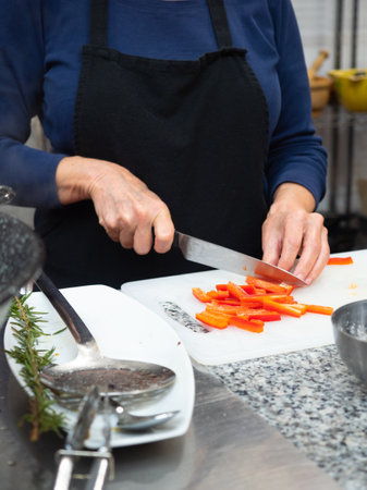 Woman's hands with knife cutting red bell pepper on white chopping board. Concept of preparing ingredients for cooking.の写真素材