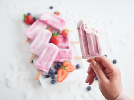 female hand holding a strawberry ice cream with a bite missingの写真素材