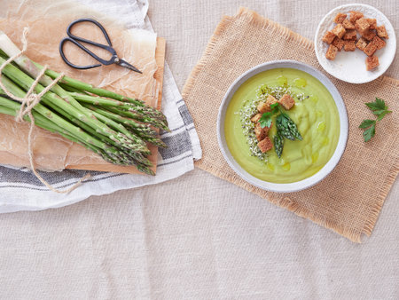 Creamy green asparagus soup with asparagus tips and toasted bread on top. Served in a bowl at the table beside a bunch of fresh wild asparagus.の写真素材