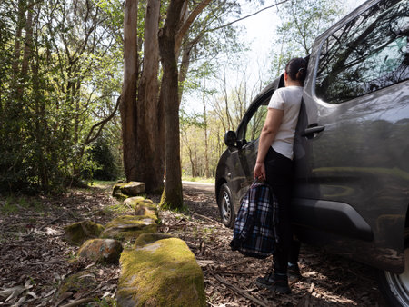 woman alone getting out of van with backpack in hand looking at the road in the forest.の写真素材