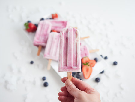 strawberry and blueberry ice cream in hand, tray with other ice cream in the backgroundの写真素材