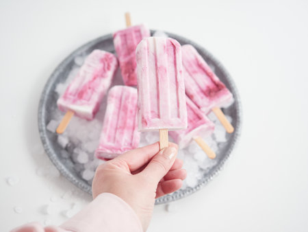 female hand taking a pink ice cream from a round silver-plated trayの写真素材