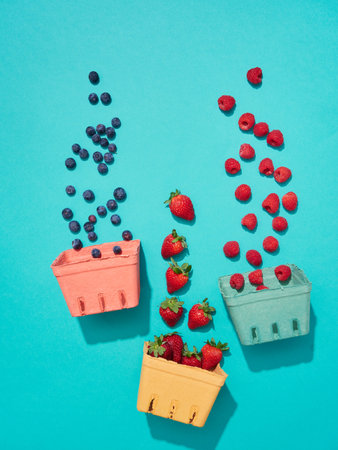 blueberries, strawberries and raspberries falling in colorful cardboard baskets for berries on a turquoise backgroundの写真素材