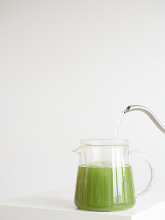 Matcha green tea in a glass jug with a splash of hot water from the kettle. Minimalist composition with copy space.の写真素材