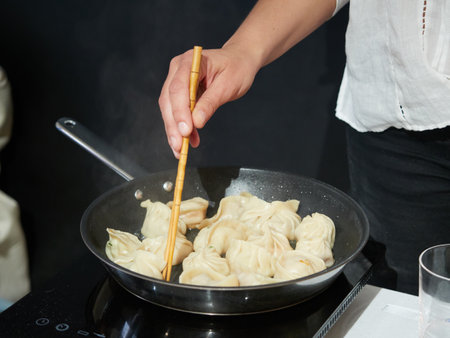 homemade dumplings cooking in a frying pan, hands with chopsticks in itの写真素材
