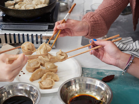 Hands of a group of friends picking up with chopsticks a homemade dumpling prepared in a cooking class. Concept of people sharing food and learning to cook.の写真素材