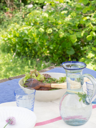 Green salad and refreshing water served at the table in the summer garden. Outdoors meals concept.の写真素材
