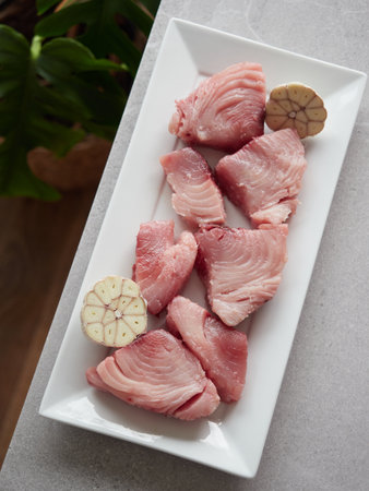 Fresh chunks of raw white tuna (Thunnus alalunga) called "bonito del norte" in Spain. On white rectangular plate with halved head of garlic. Top view on gray marble countertop.の写真素材