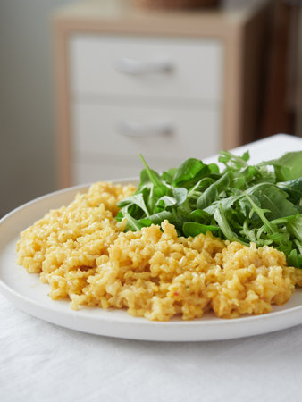 close-up view of a portion dish with yellow rice and green salad leaves on the kitchen tableの写真素材