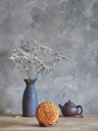 Front view of moon cake, in background vase with branches of dried flowers and small teapot. Mid-autumn festival composition, copy space.の写真素材