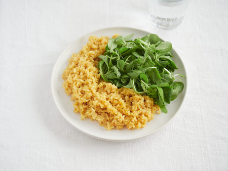 plate with yellow rice and salad greens, arugula and lamb's lettuce, on linen tablecloth on the...