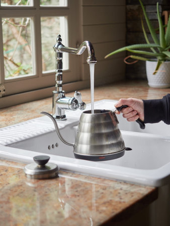 Women pouring water from a kettle into a sink in a modern kitchenの写真素材