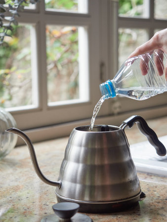 Pouring water from a plastic bottle into a kettle on the kitchen tableの写真素材