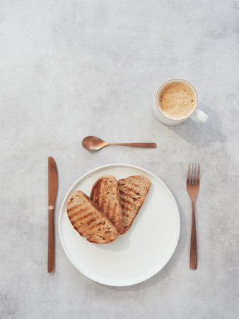 Top view of two toasted bread sandwiches on white plate with cup of coffee on gray backgroundの写真素材