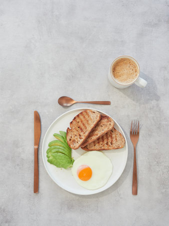Breakfast with fried egg, avocado and toasts on white plateの写真素材