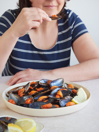 Close-up of woman eating mussels with lemon on white plateの写真素材