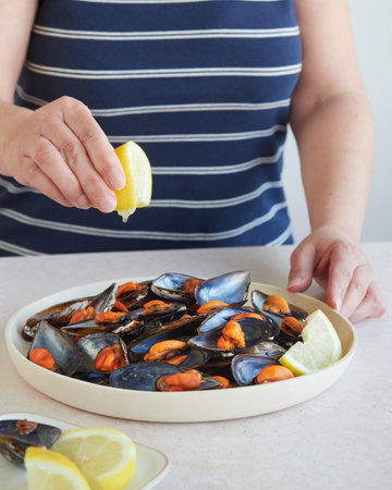 Closeup of woman's hands cooking mussels with lemon on white plateの写真素材
