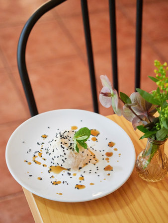 Italian panna cotta dessert with sesame and mint leaf on white plate served on restaurant table, vase with decorative flowers.の写真素材
