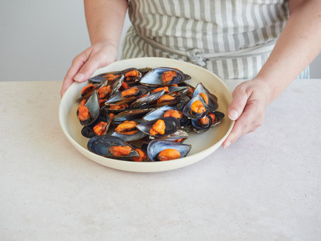 Woman's hands holding a plate of fresh mussels in the kitchenの写真素材