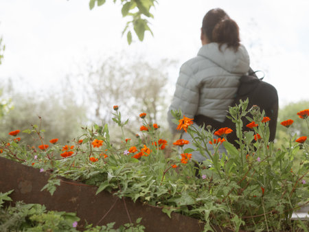 Woman on her back with backpack in front of a garden fence with orange flowers.の写真素材