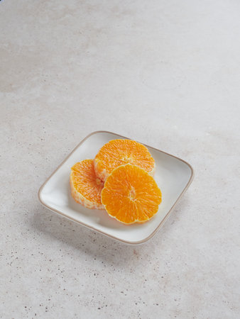 three juicy slices of fresh orange on a square plate on a cream-colored stone backgrounds. Copy space.の写真素材