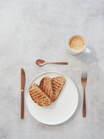 Top view of three slices of toast on white plate with coffee cup and bronze-colored silverware on...