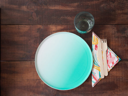 Single-use utensils for eating outdoors or at a picnic on wooden table. Disposable empty green...